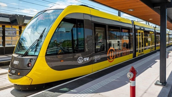 A yellow and black tram of the province of Utrecht stands at a station.
